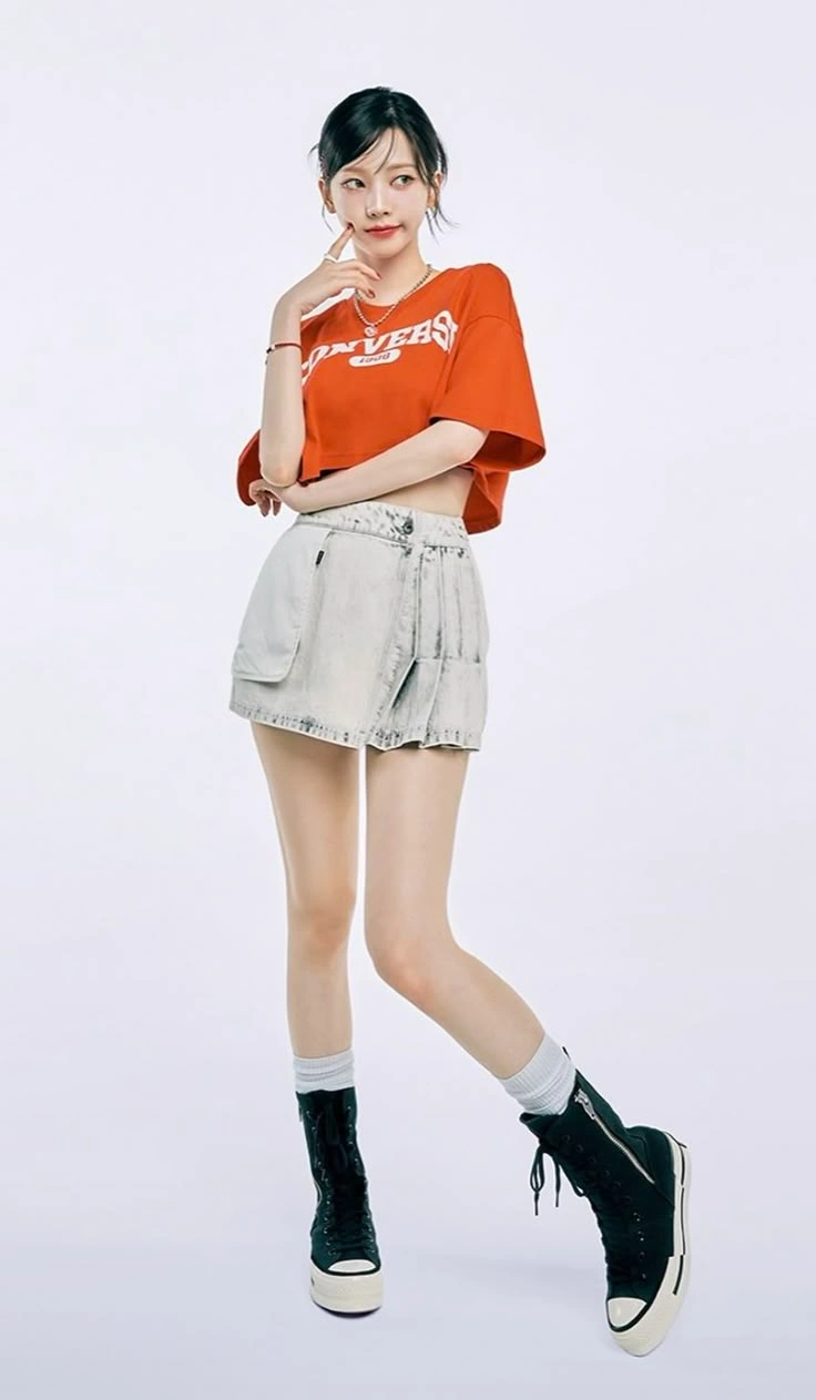주황색 크롭 티와 연청 스커트를 입은 여성이 흰 배경에서 포즈를 취하고 있다.